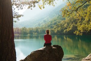 Person sitting calmly by a peaceful lake, symbolizing the tranquility and relaxation achieved through hypnotherapy for anxiety relief.