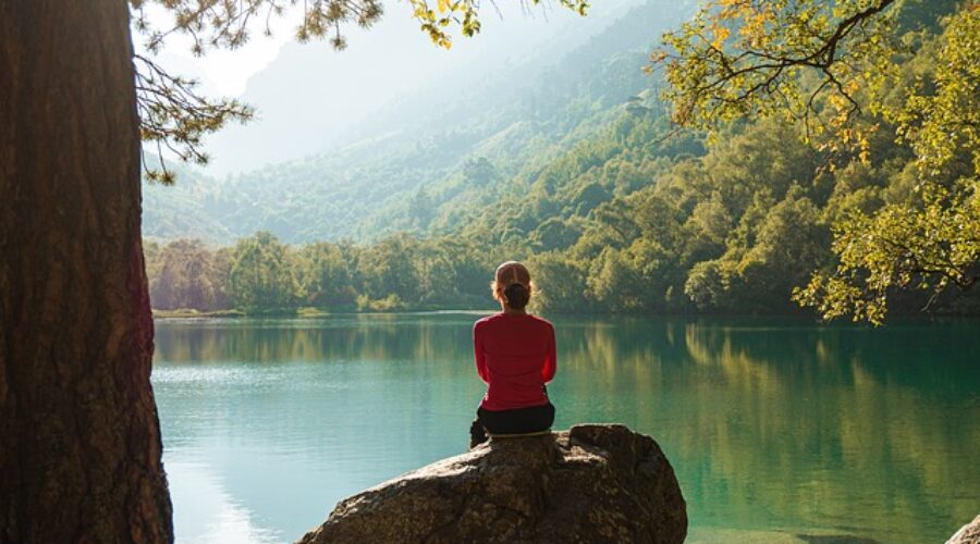 Person sitting calmly by a peaceful lake, symbolizing the tranquility and relaxation achieved through hypnotherapy for anxiety relief.